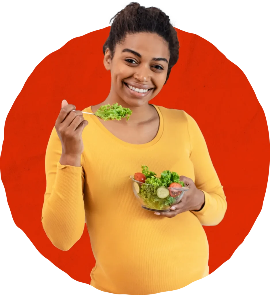 A smiling pregnant woman in a yellow top holds a bowl of salad with lettuce, tomato, and cucumber, holding a forkful of greens. A red circle is in the background.