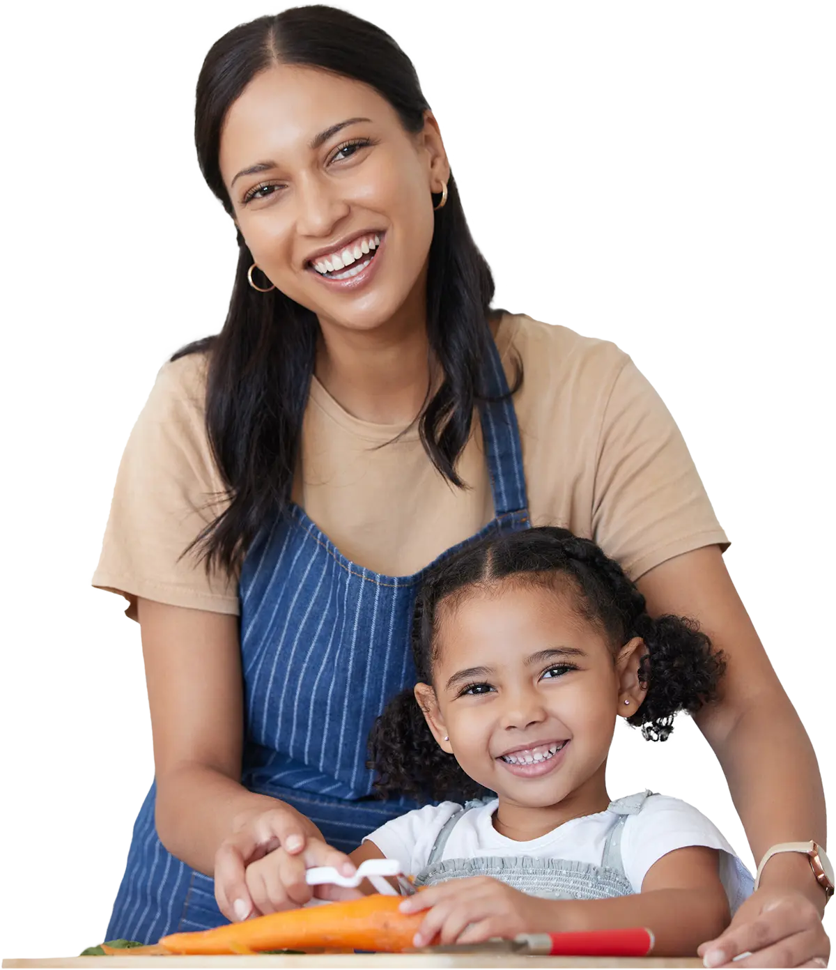 A smiling woman in a striped blue apron and tan shirt sits with a young girl, who is also smiling, as they cut vegetables together at a table.